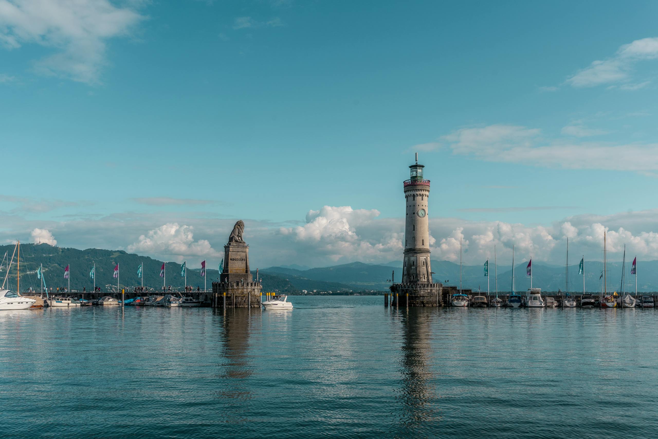 Peaceful scene of a lighthouse and boats on a calm lake with a mountain backdrop.